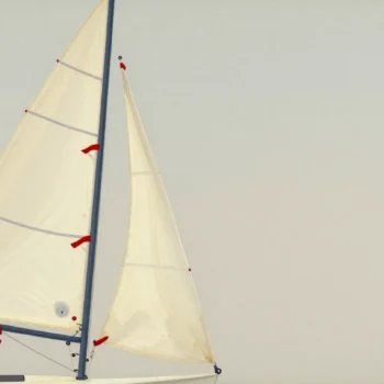 Three red ribbons on a sail, two streaming smoothly and one fluttering upward, a hand ready on the rope.