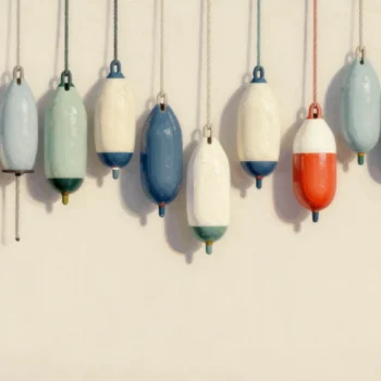 Painted fishing buoys hanging on a harbor wall in color groups, a few bare, one red buoy among the blue