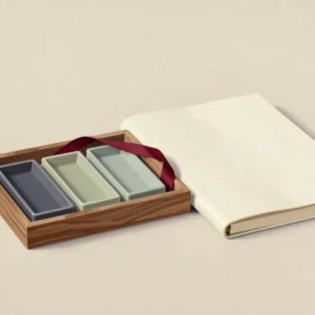 Three empty rectangular ceramic dishes in a wooden tray beside a blank cream folio and vermilion ribbon.