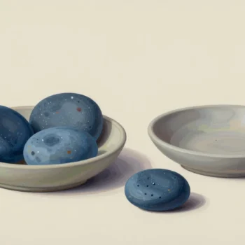 Three blue stones in a pale shallow bowl, an empty bowl and one separate blue stone.