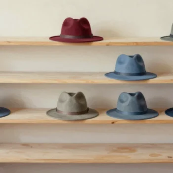 Red, blue and gray felt hats share different levels of a wooden display shelf.