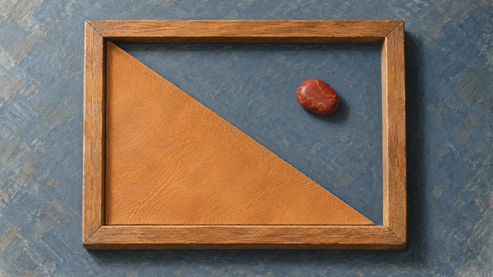 A wooden frame with a leather triangle in one corner and a red stone inside the frame but outside the triangle.