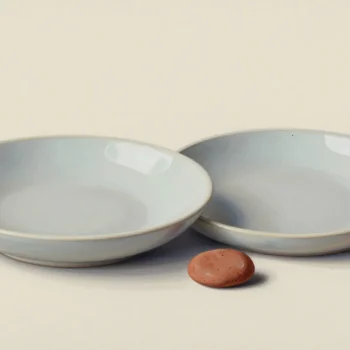 Two empty pale ceramic bowls beside a small terracotta pebble.