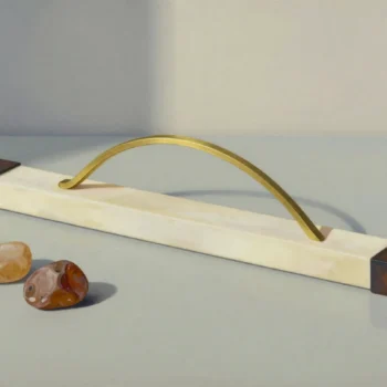A curved brass strip over a straight ivory bar between dark wooden end blocks, beside two ochre stones.