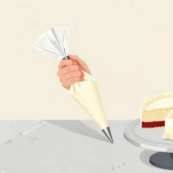A baker's hand fitting a star nozzle to a piping bag, a round nozzle set aside beside a half-decorated cake