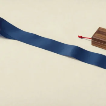 A long blue ribbon with a notched end lies beside a closed walnut box and red cord.