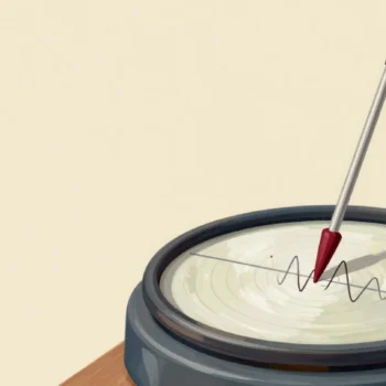 A seismograph drum with a calm ink line and one sharp spike, a fingertip pausing beside the spike