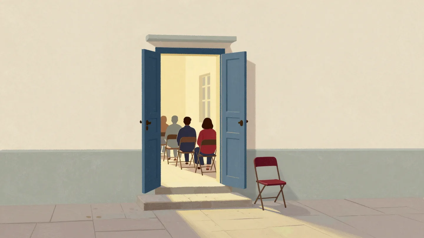 The open door of a village hall at dusk, warm light on the steps and one empty folding chair near the entrance.