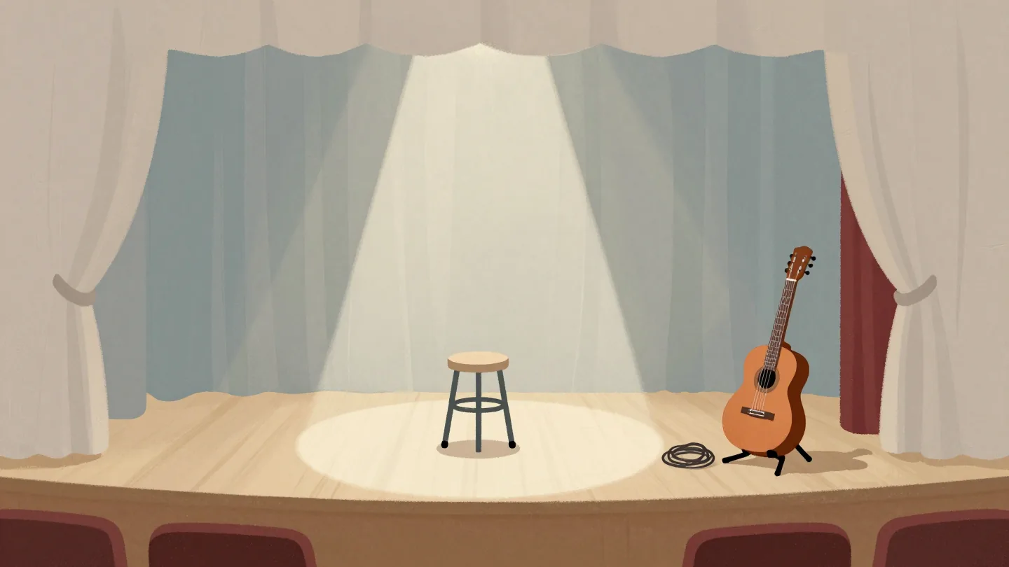 View from a theater's wings of a lit stage with one stool, and a spare guitar on a stand just inside the curtain.