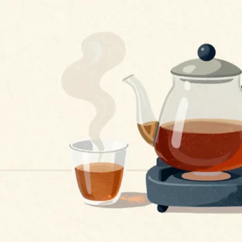 A glass coffee pot on a hotplate in a quiet diner, one freshly poured cup beside it with a thin wisp of steam.