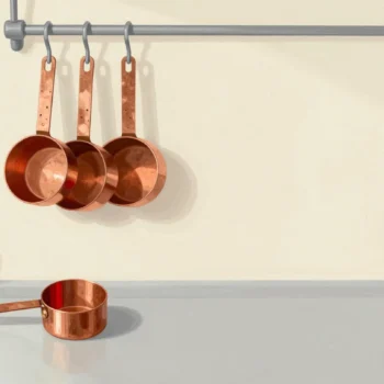 A nested set of copper measuring cups on a hook, with one stray cup from a different set lying on the counter below.