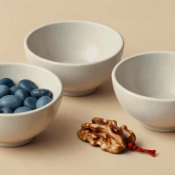 Three ivory bowls hold blue pebbles or remain empty, beside a walnut piece and red cord.