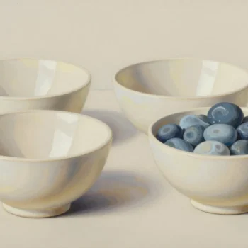 Four pale ceramic bowls in two pairs, three empty and the front-right bowl filled with blue pebbles.