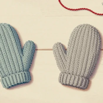 Two identical mittens knitted from the same pattern, one still on the needles