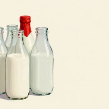 Rinsed empty milk bottles on a doorstep at dawn waiting for reuse, one still wearing a red foil cap.