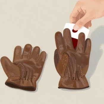 Two nearly identical brown leather gloves on a hall table, both for the left hand, a hand hovering above them.