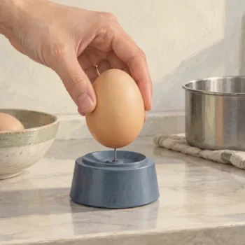 An egg poised on a small piercer before cooking