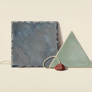 A solid slate-colored rectangular tile beside a sage triangular tile, a loose cream cord and a red pebble.
