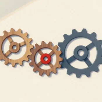 Three interlocking gears on a pale board, two wooden and one gray, the middle gear with a red center.