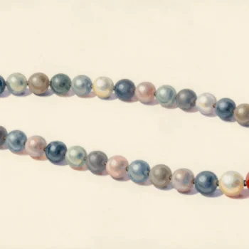 Two pearl strands side by side on velvet, matched bead for bead, one pearl in the second strand a warmer shade.