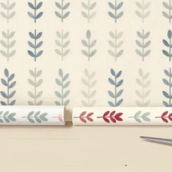Two strips of matching leaf wallpaper side by side on a floor, one with a single red leaf that differs.