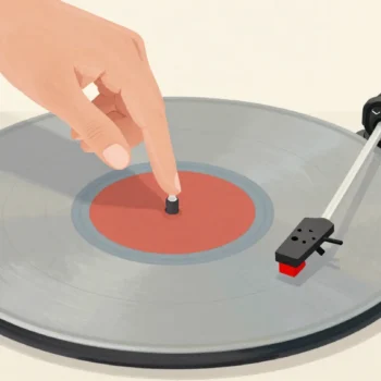 A hand lowering a record player's needle just before a scratch on a spinning record with a red center