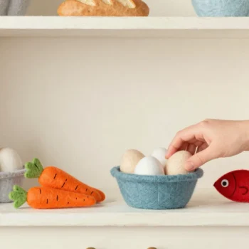 A play kitchen shelf stocked with handmade felt food, many eggs, fewer carrots and one red felt fish.
