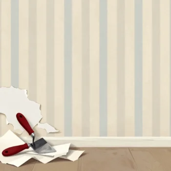 A wall with torn strips of old wallpaper still clinging, a red-handled scraper below