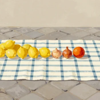 A checkered cloth spread on market cobblestones as a makeshift stall, with a short row of lemons and one blood orange.