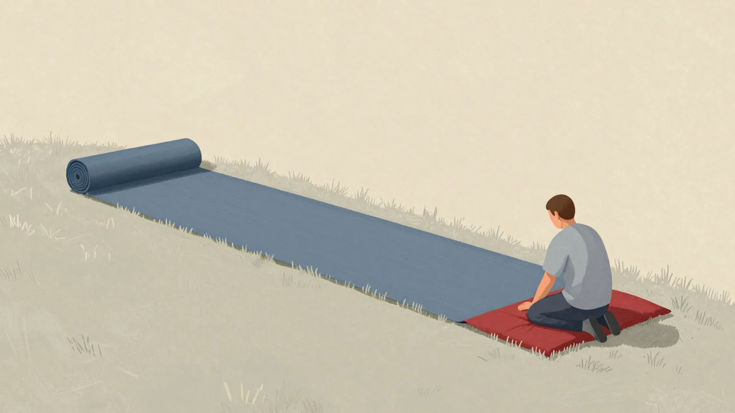 A gardener seen from behind slowly rolling a long strip of turf back up across a lawn, most of it still flat.