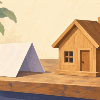 A folded paper shelter stands beside a permanent wooden house on a workbench