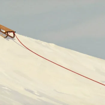 A heavy sled hauled almost to the top of a snowy slope, its red rope trailing back down