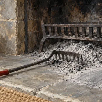 A hearth ash rake beside settled ashes from an earlier fire