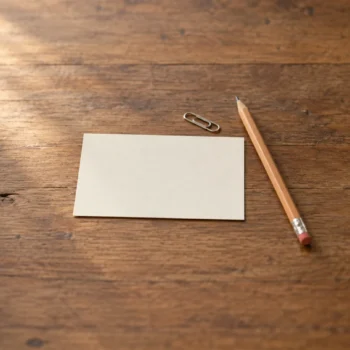 One blank cream reference card beside a plain pencil and small paper clip on a wooden desk.