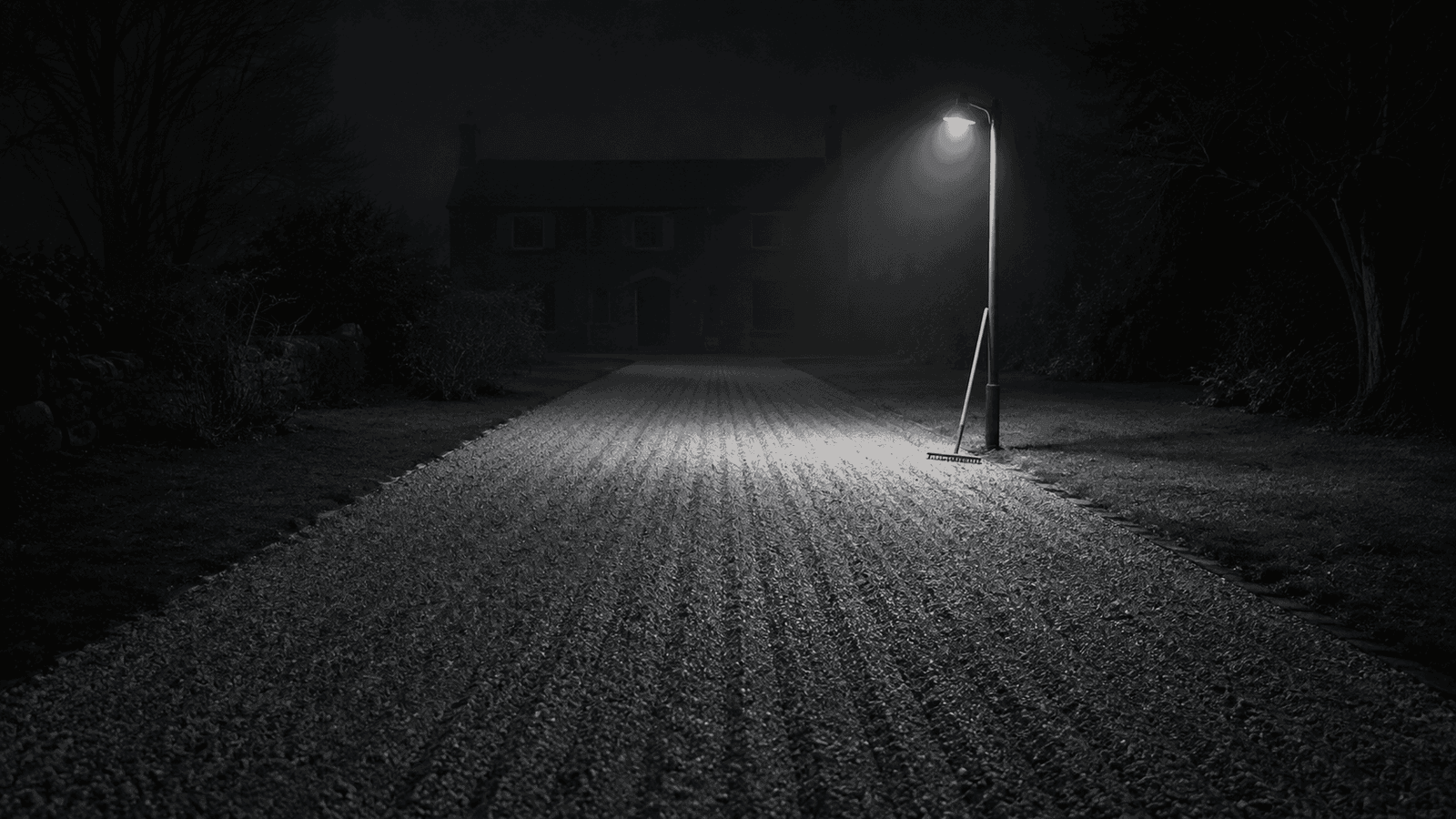 A gravel driveway raked into flawless parallel lines at night with no car and a dark house