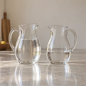 Two matching glass pitchers contain water at different levels on a quiet kitchen counter.