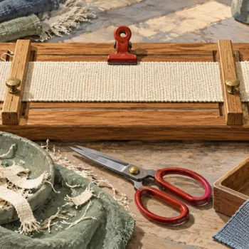 Gouache painting of a frayed woven strip held between wooden guides beside red scissors and trimmed fibers.
