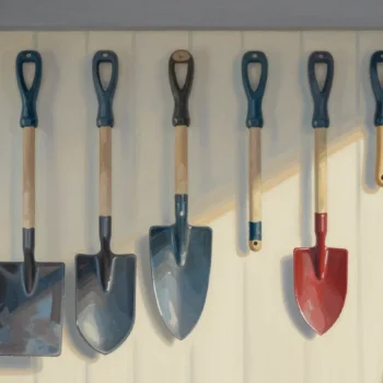Gouache painting of a row of worn garden tools with one spotless untouched red trowel in the middle