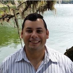 A man smiling with water in the background.