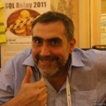 A smiling man giving a thumbs up in front of a SQL Server 2011 poster.