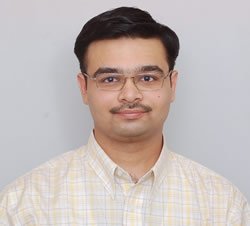 A man with glasses and a mustache wearing a checkered shirt.