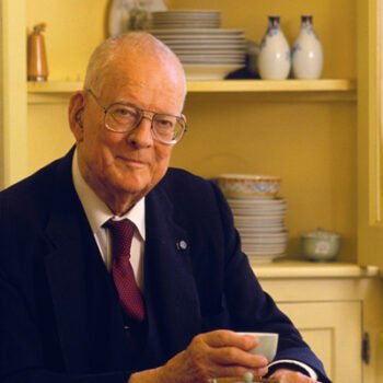 A man in a suit and red tie, drinking tea.