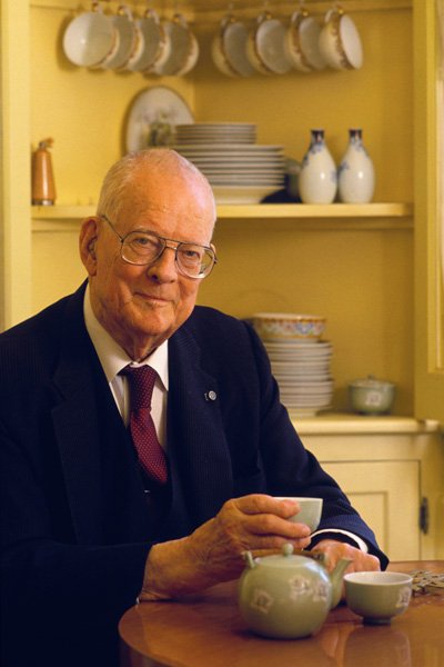 A man in a suit and red tie, drinking tea.