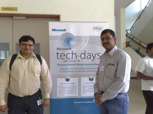 Two men standing in front of a Microsoft and Infosys banner.